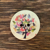1 1/8 inch round wooden button with two holes. Feathering a flowering tree.