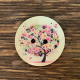 1 1/8 inch round wooden button with two holes. Feathering a flowering tree